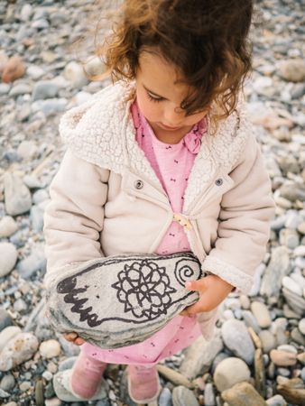 Girl holding painted stone while playing on beach