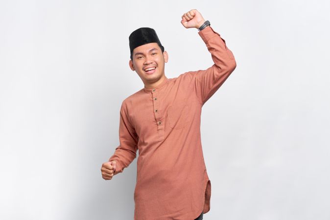 Joyful Muslim man in kufi head wear with his hands up