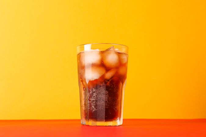 Glass of cold cola against color background, space for text