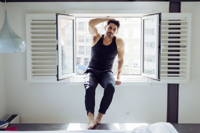 Young happy man sitting on window