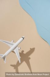Top view of model airplane with shadow over beige and blue water beach scene 0K3vA0