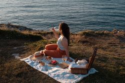 Woman with glass of drink on picnic mat looking at sea and mountains