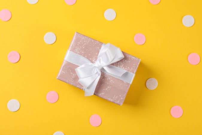 Gift box with bow on decorated yellow background, space for text