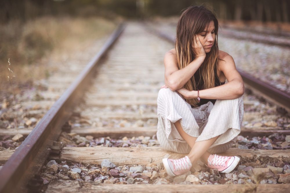 Long haired woman sitting on railways overgrown with dry grass