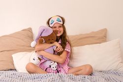Girl in bedroom embracing teddy bear with joy.