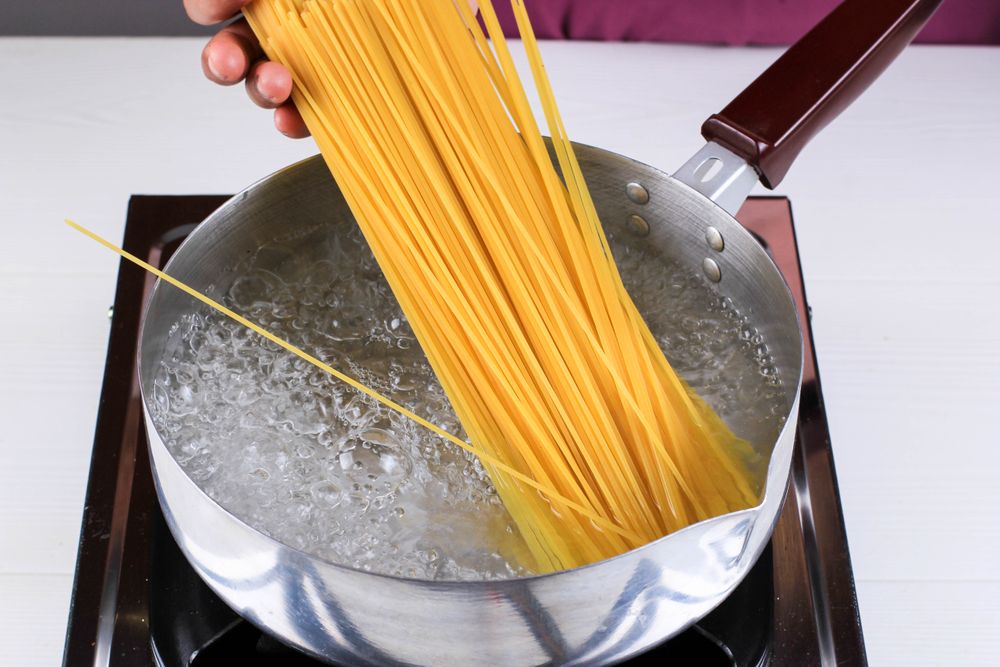 Women Cooking Spaghetti in Pan of Boiling Water in the Kitchen
