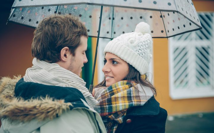 Couple looking at each other lovingly under the umbrella on an autumn rainy day