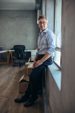 Middle aged man leaning against windowsill in office