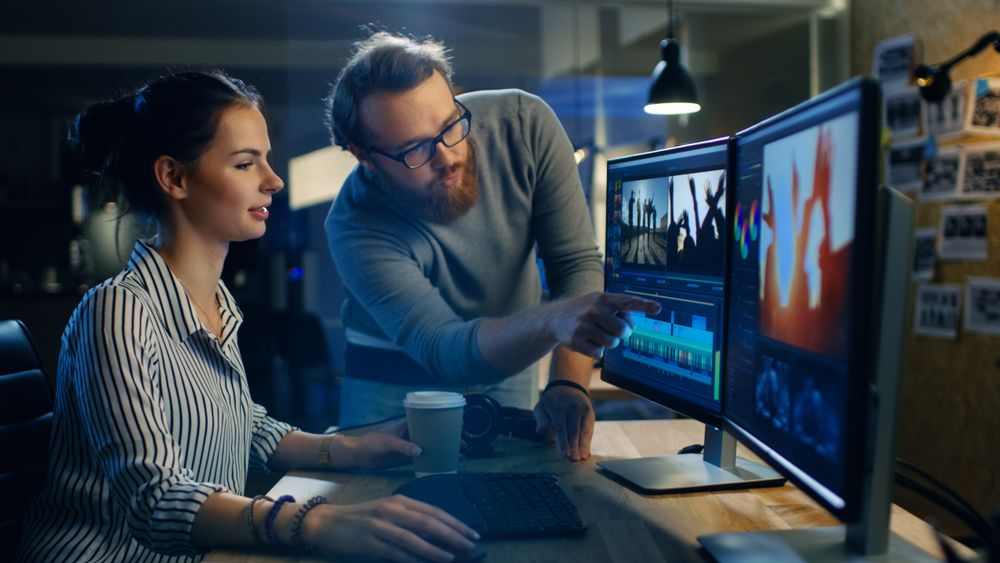 Female Video and Sound Editor Works With Her Male Colleague on a Project on Her Personal Computer with Two Displays.