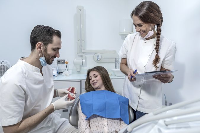 Young woman is sitting in dental chair in clinic, office with dentist showing jaw