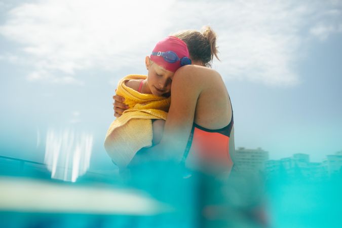 Girl feeling cold after swimming and mother soothing her with a hug