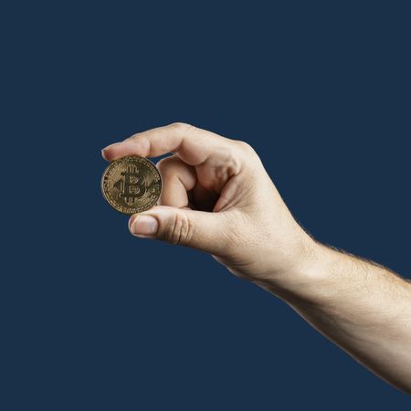 Hand holding a Bitcoin coin on a blue background.