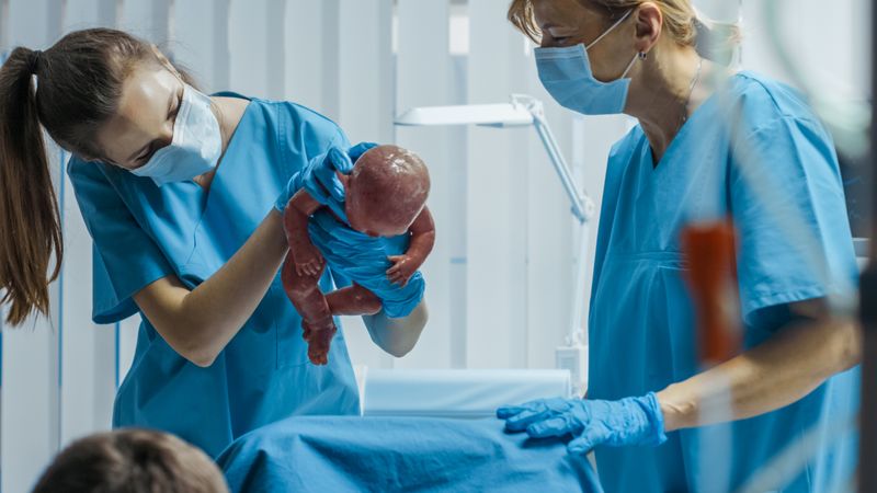 In the Hospital Woman in Labor Pushes to Give Birth, Baby Comes out, Obstetricians Assist Delivery, Husband Holds Supports His Wife