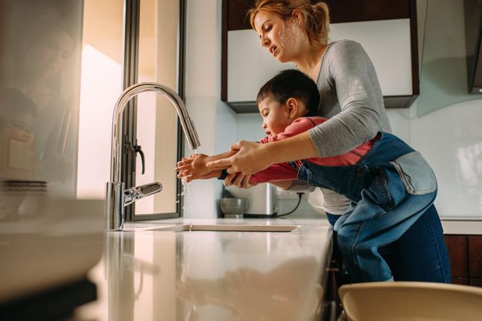 Cute son washing hands with mother in the sink after cooking