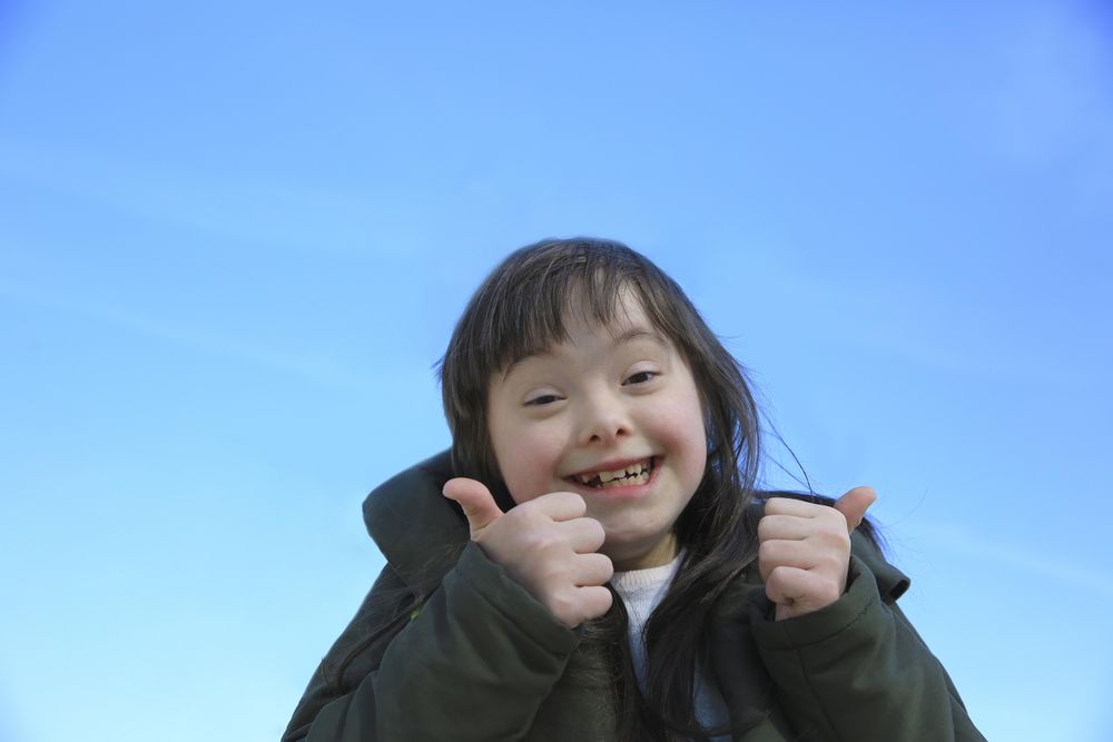 Little girl giving a thumbs up and smiling against a bright blue sky