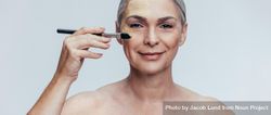 Beautiful woman with gray hair applying foundation on face with makeup brush 5rq3l0