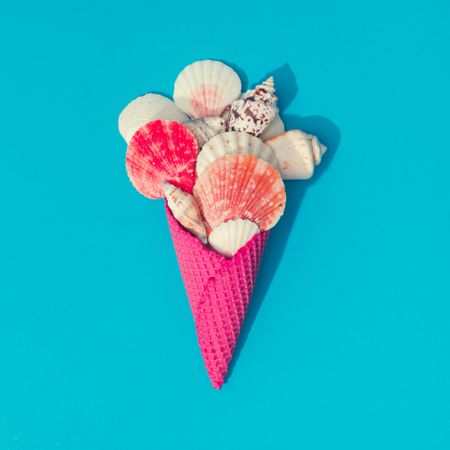 Sea shells in pink waffle cone on bright blue background