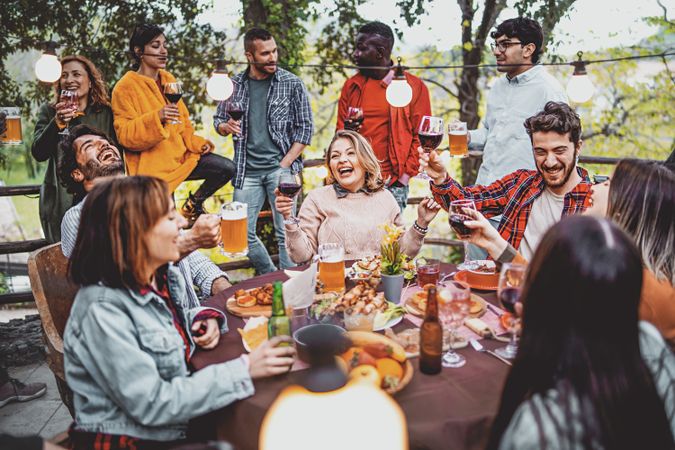 Young friends having fun drinking beer and wine on balcony at farmhouse dinner picnic party