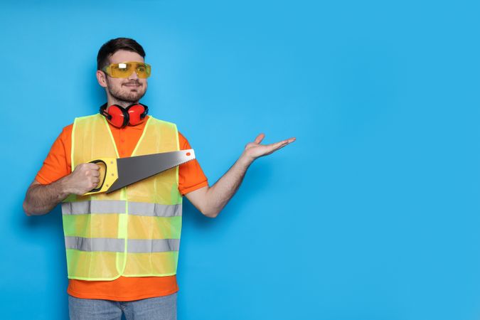 Engineer in glasses with saw in hands on blue background, space for text