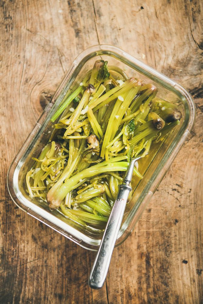 Mediterranean spinach stem dish in square glass container on wooden board with serving fork