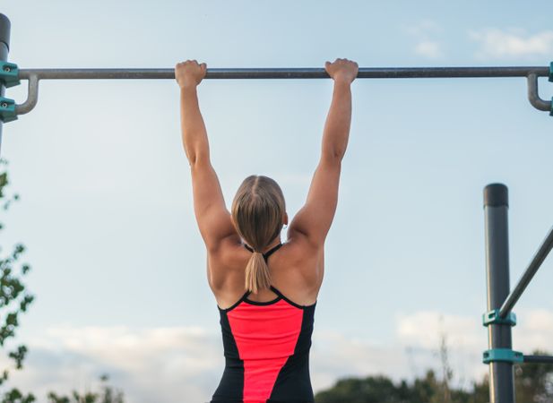 back view of a woman athlete doing pull ups on a bar outdoors, calisthenics