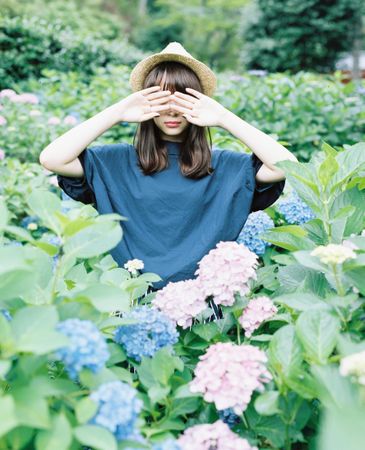 Woman hiding her eyes with her hand standing on blue and purple flower field