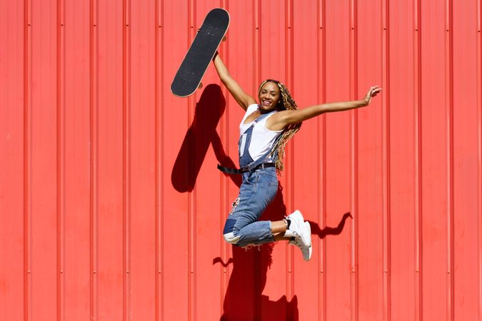 Woman smiling and jumping for joy in front of a red wall with skateboard