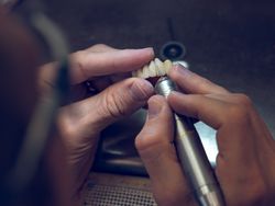 Crop dental technician grinding artificial teeth
