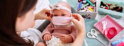 Girl trying on her doll a mask that she is sewing