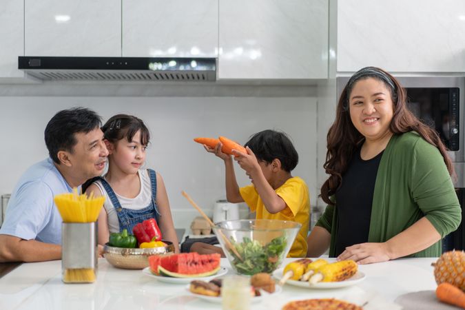 Happy Asian family in the kitchen together with son playing with carrots