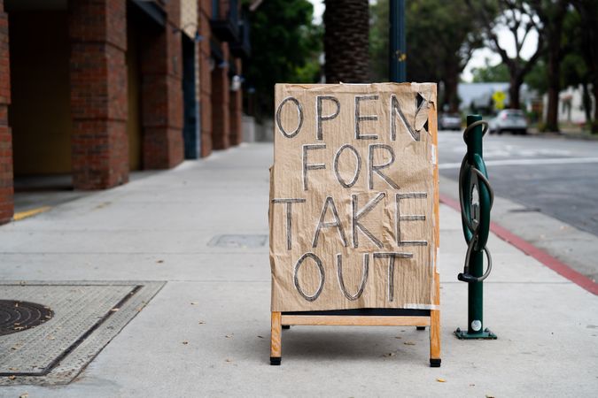 Sandwich board on city sidewalk with “open for takeout” hand lettered