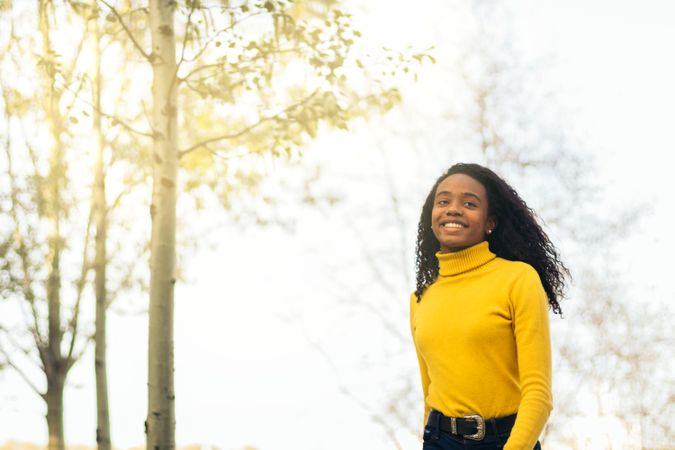 Black woman in yellow, walking and smiling in a park