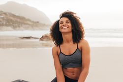Happy woman sitting on beach in workout gear