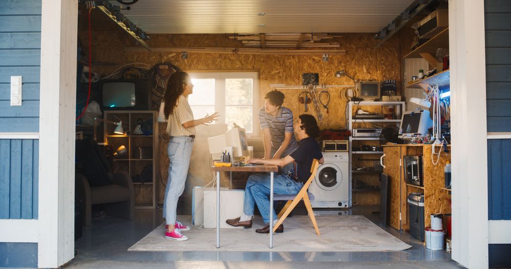 Diverse Team Of Three Young Tech Startup Company Founders Working In Retro Garage, Using Old Desktop Computer.