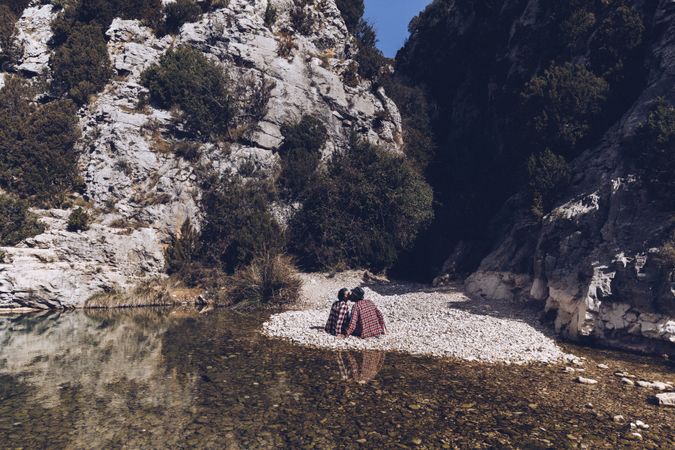 Positive woman and man resting and kissing on stone shore near river