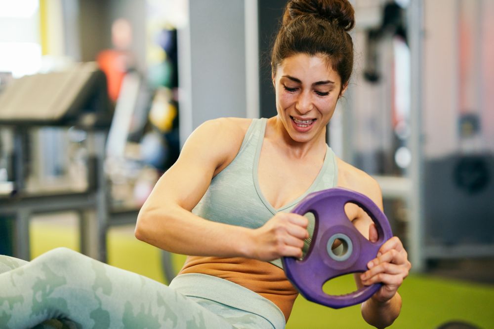 Woman exercising her abs with twists in gym on mat with weight