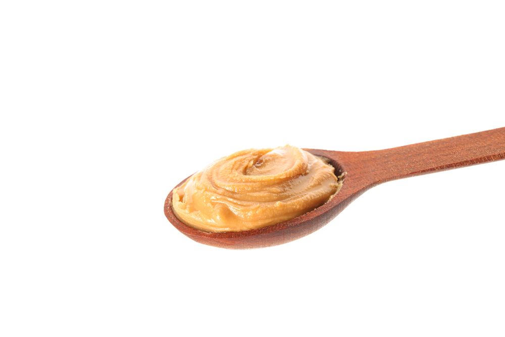 Creamy peanut butter in wooden spoon isolated on bright background, closeup. A traditional product of American cuisine