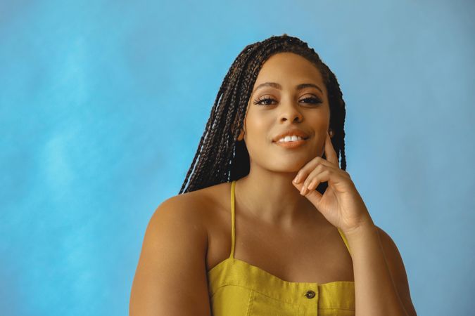 Portrait of smiling female with long braided hair with hand on chin in yellow shirt