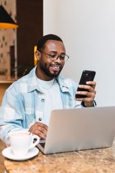 Cheerful Black man browsing smartphone in cafB