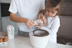 Young mother mixing dough with young daughter helping in the kitchen