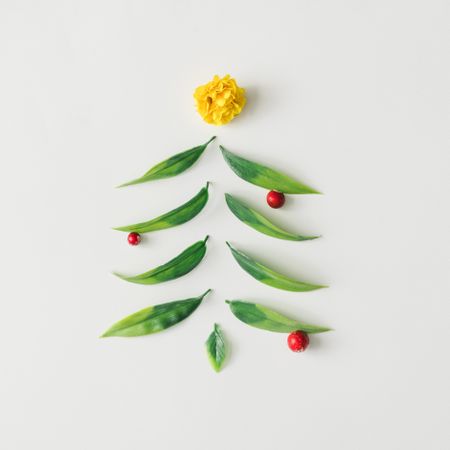 Christmas tree made of green leaves with red berries, topped with yellow flower on light background