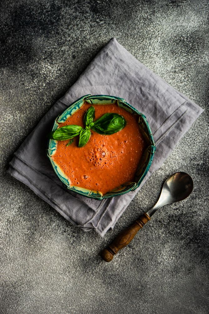 Top view of traditional Spanish tomato soup Gazpacho with basil on grey napkin