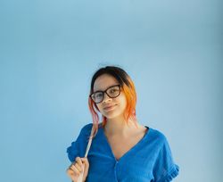 A young female with orange hair looks at the camera with a smile, on a plain blue background