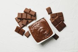 Bowl with chocolate and chocolate pieces on light background
