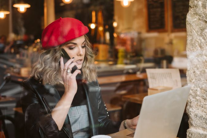Woman with laptop using smartphone in cafe