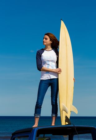 Woman with surfboard standing on roof of car