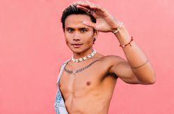 Male in open overalls looking at camera posing against a pink wall