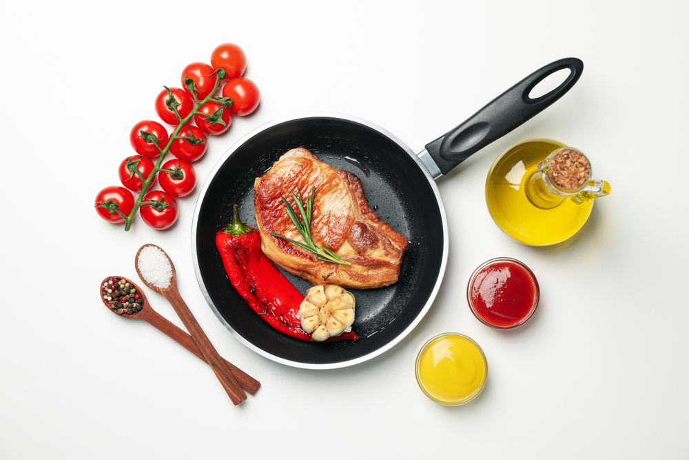 Pan with fried steaks and ingredients for cooking on blank background, top view