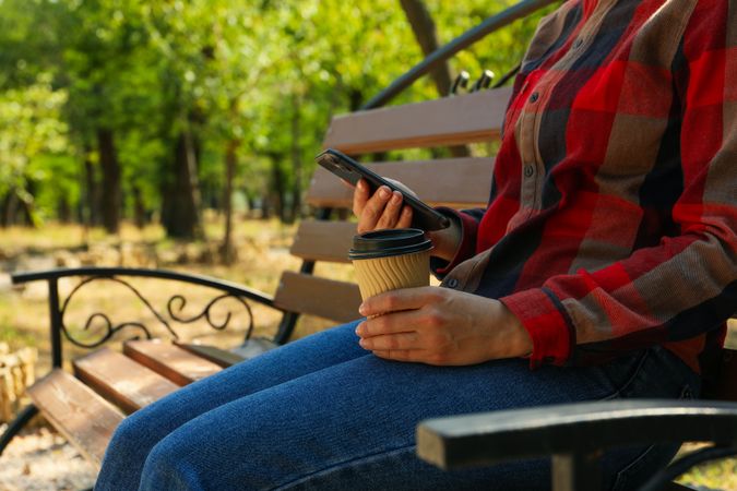 Woman in jeans and shirt hold paper cup and phone outdoor
