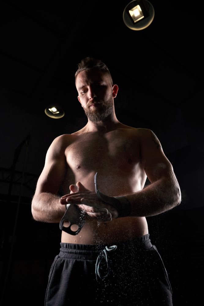 Muscular sportsman preparing hands with chalk for exercise